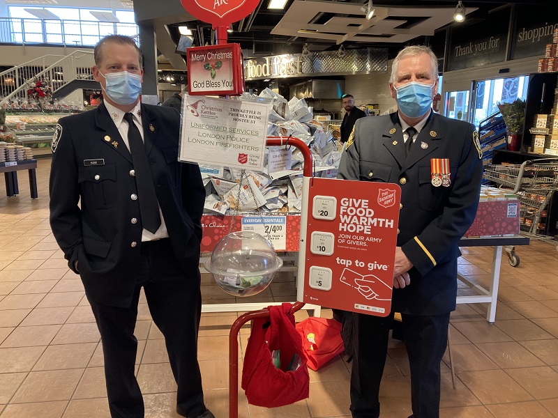 Two officers from fire and police services stand alongside Salvation Army kettle