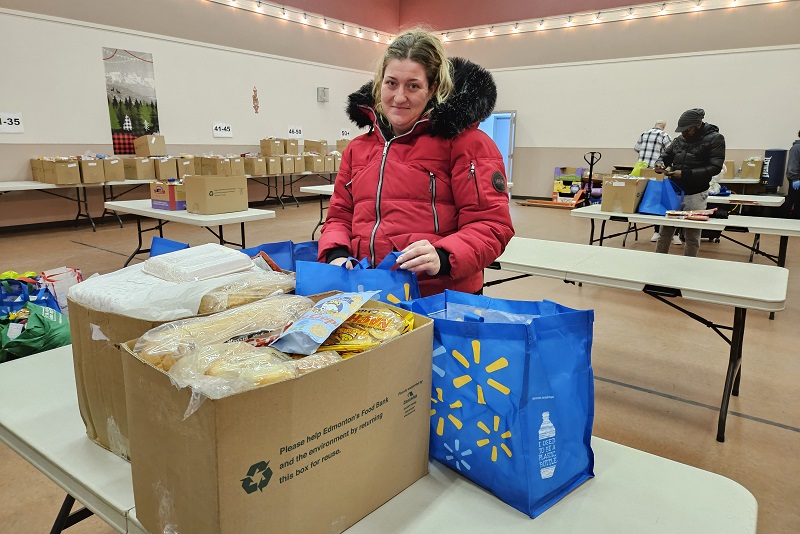 food bank client stands in from of food boxes