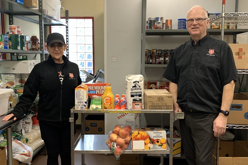 Two Salvation Army workers stand alongside trolly of healthy snacks such as oranges, apples and juice