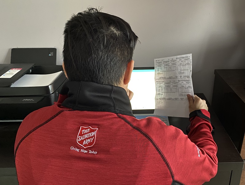Salvation Army worker sits in front of computer holding a tax form