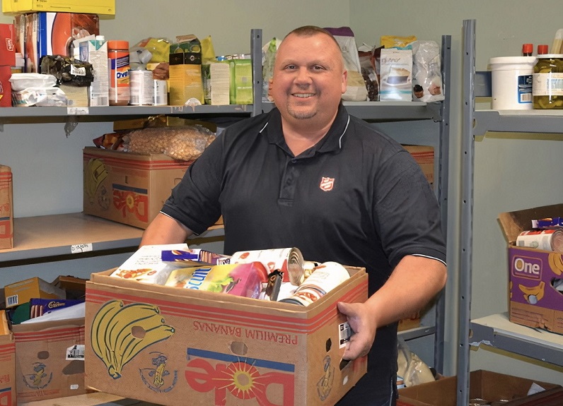 Salvation Army worker holds box of food in food storage room
