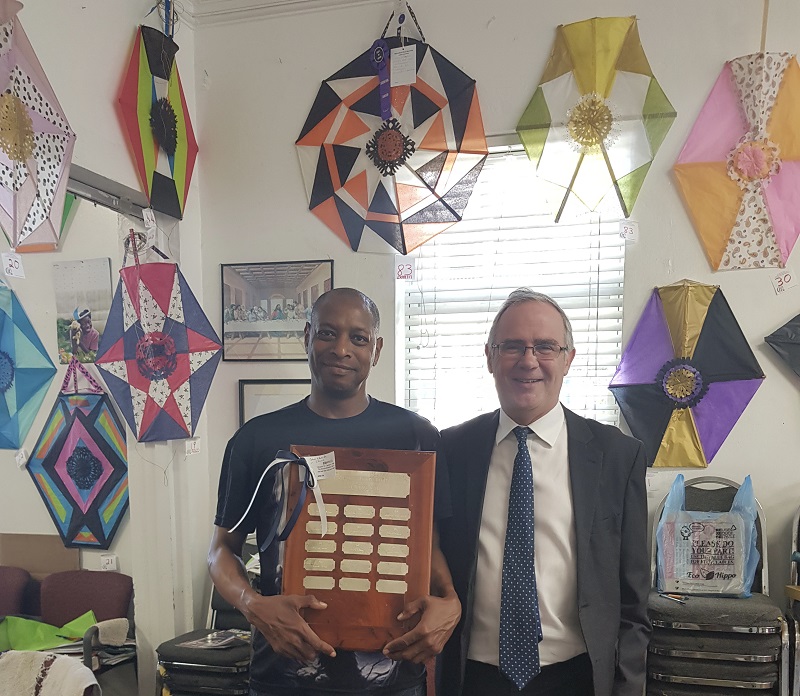 Dion holds award, with kites in the background. Governer of Bermuda stands alongside him