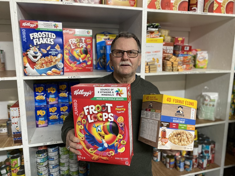 Food bank worker holds food items in front of food bank shelves