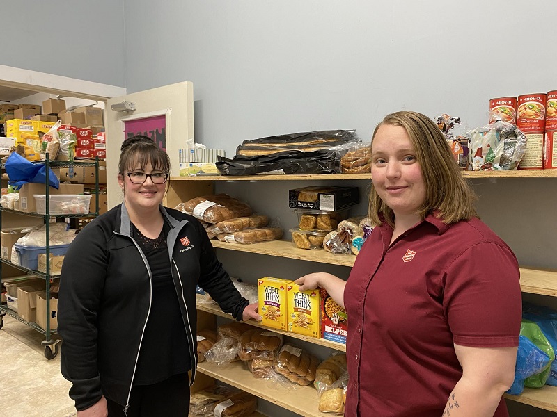 Two food bank workers stand aside food bank shelves