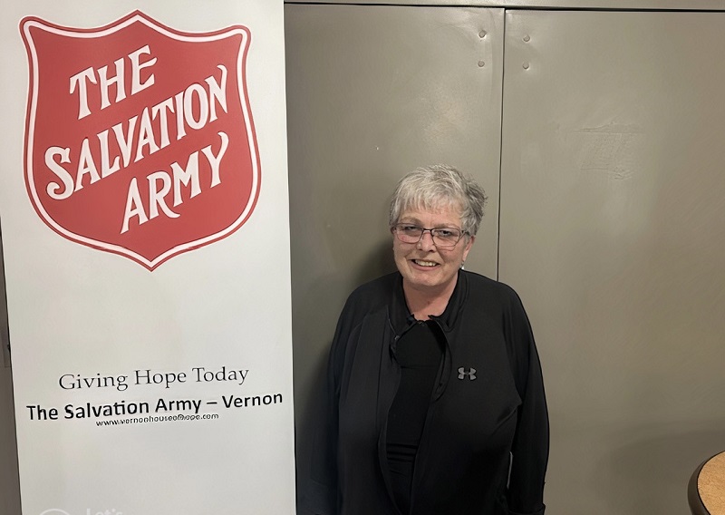 Terry Lynn stands by Salvation Army sign with shield and Giving Hope Today