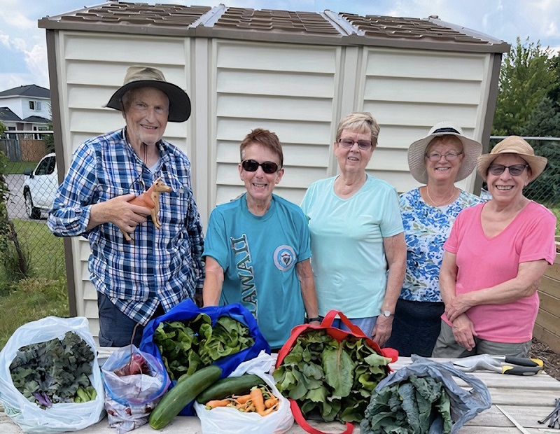 Community garden members stand behind table with various home-grown vegetables