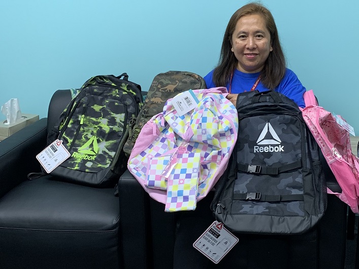 Salvation Army worker holds five backpacks for distribution