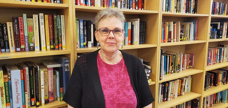 Alison stands in front of book shelves at thrift store