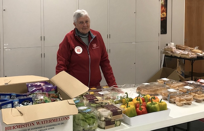 Food bank worker stands behind tables of food for distribution