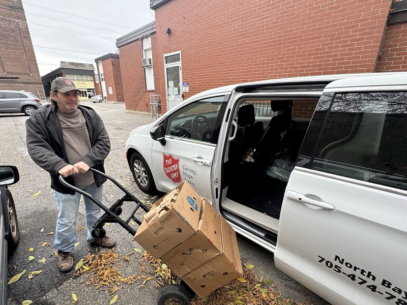 Volunteer stands beside van ready to load boxes of school lunches