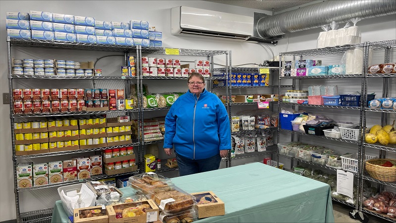 Salvation Army worker stands in front of food bank shelves