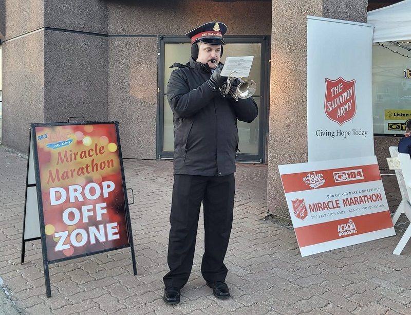 Salvation Army worker plays Christmas carols on trumpet in front of drop off zone