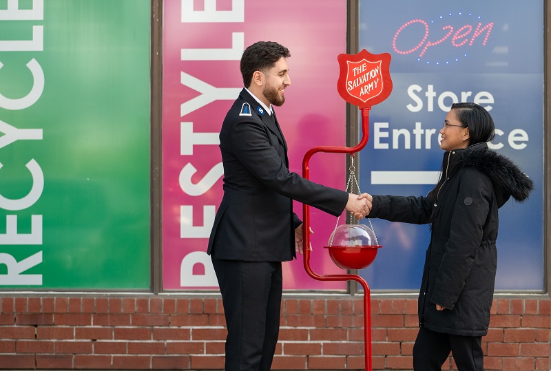 worker in uniform shakes hand with donor in front of kettle stand