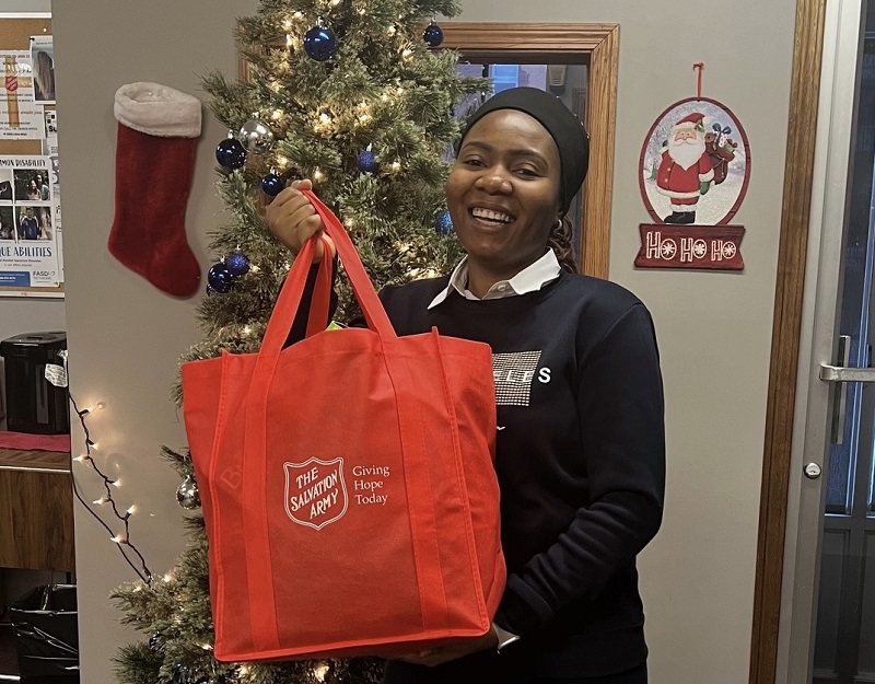 Obehi stands in front of Christmas tree holding hamper bag