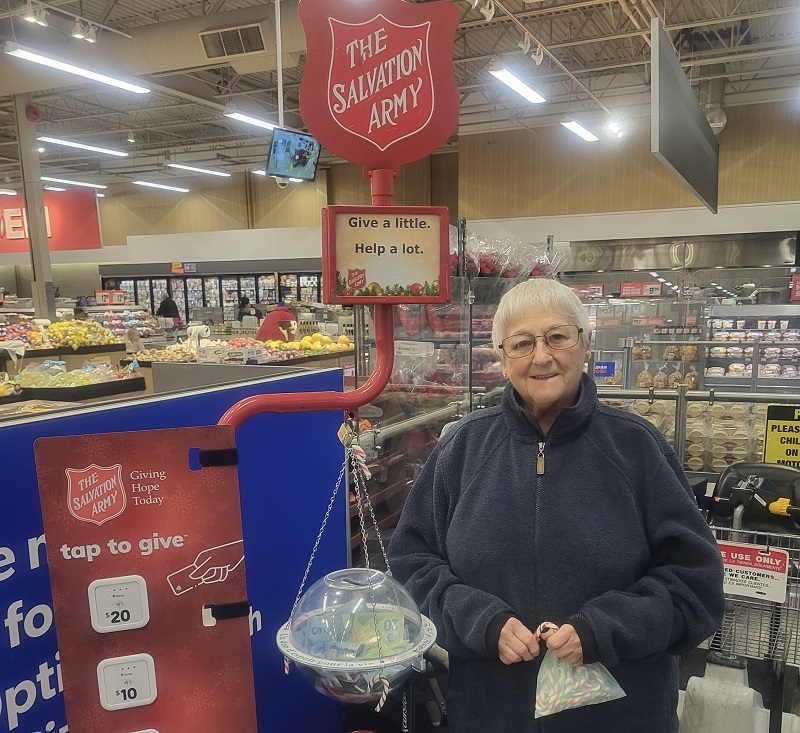 Pauline stands in grocery store beside Christmas kettle