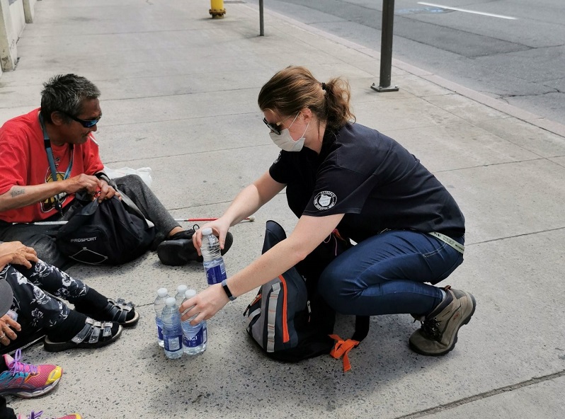 Outreach worker distributes bottled water to people sitting on the street