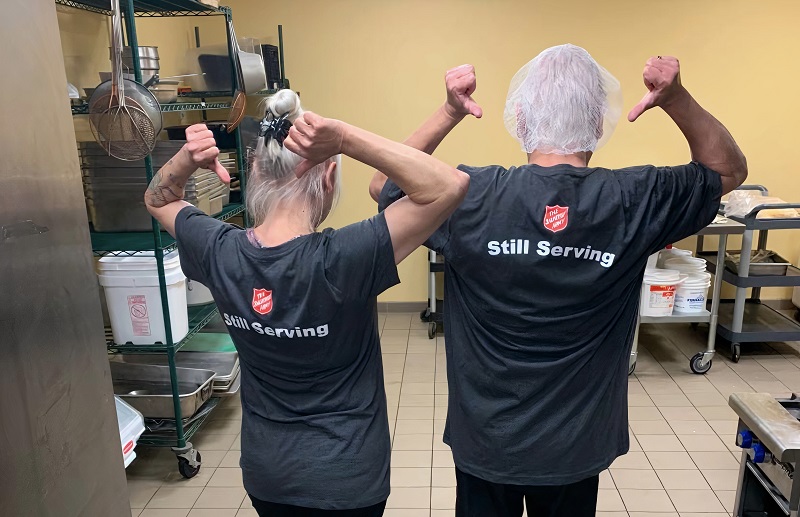 Salvation Army kitchen staff with shirts declaring "still serving"